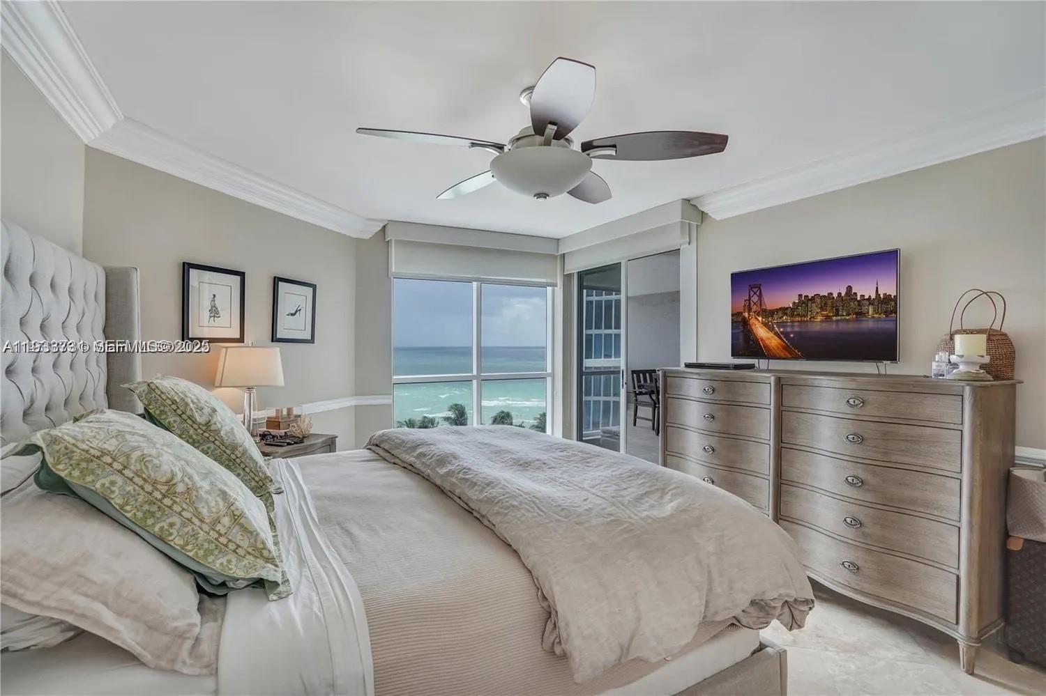 A bedroom features a bed, a dresser with a television, and a view of the ocean — 6767 Collins # 901, Miami Beach FL 33141, MIAMI BEACH, FL