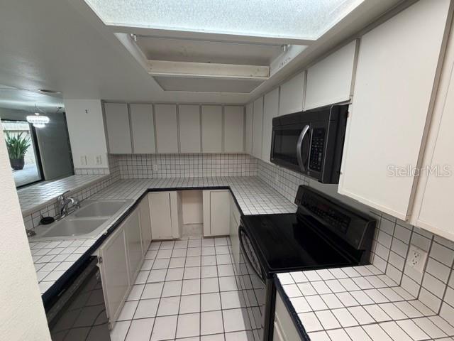 A kitchen features white cabinets, tiled countertops, a black microwave, and a black electric range — 28 CASARENA COURT, WINTER HAVEN, FL