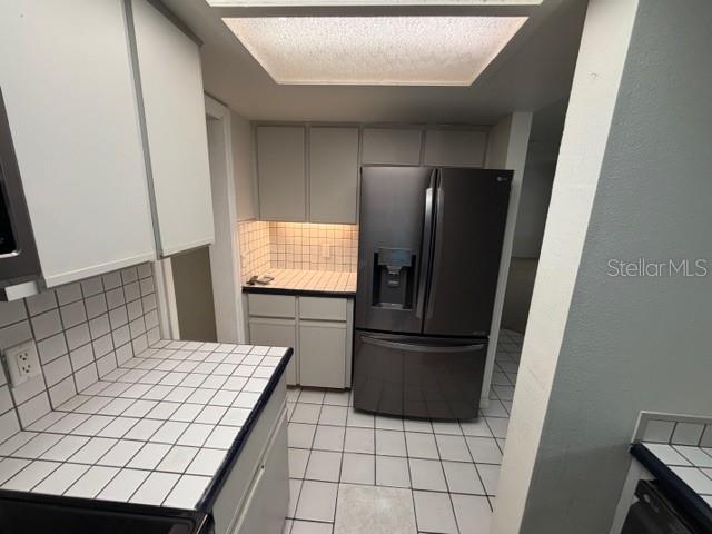 A kitchen features white tiled countertops, light gray cabinetry, and a dark stainless steel refrigerator — 28 CASARENA COURT, WINTER HAVEN, FL