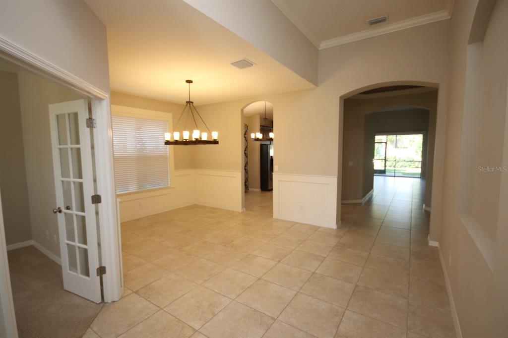 A dining room with tile flooring, wainscoting, and a chandelier, adjacent to a hallway — 8827 SENTIERO DRIVE, LAND O LAKES, FL