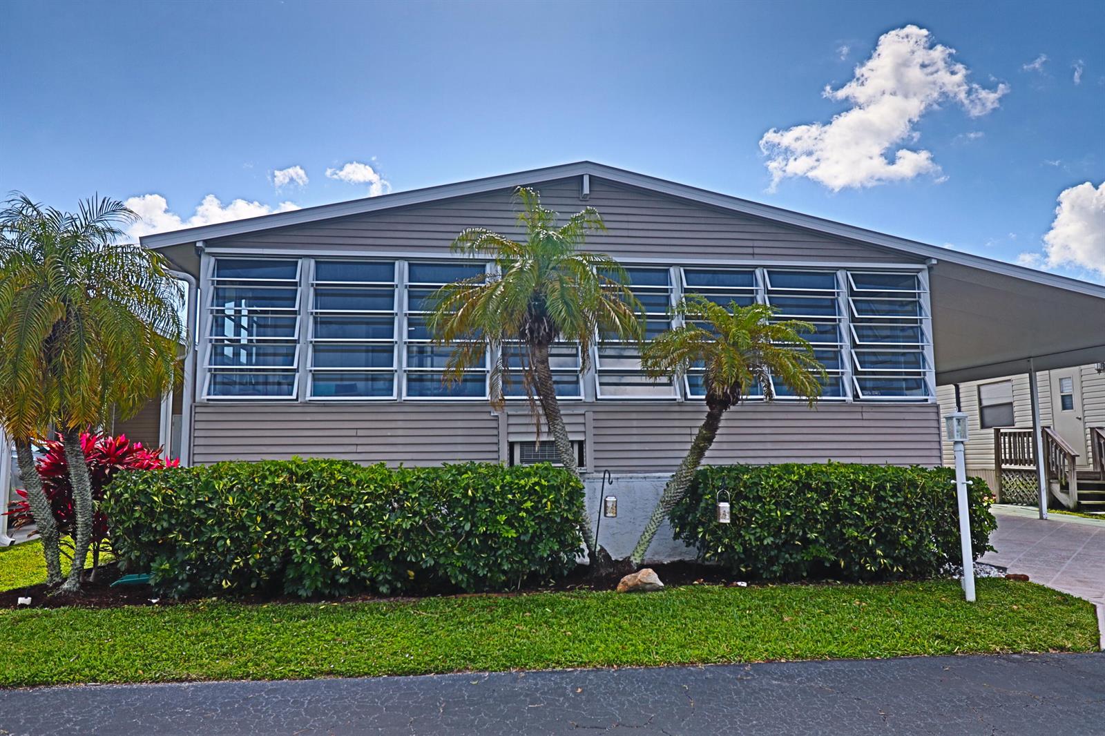 The exterior of a single-story home features horizontal siding, jalousie windows, and two small palm trees — 9002 Fomento Bay, Boynton Beach FL 33436, BOYNTON BEACH, FL