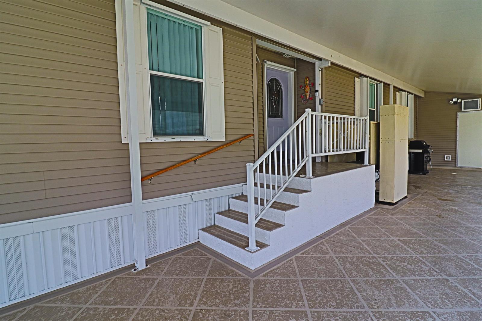 An exterior view of a mobile home featuring a covered patio, stairs, and white railing — 9002 Fomento Bay, Boynton Beach FL 33436, BOYNTON BEACH, FL