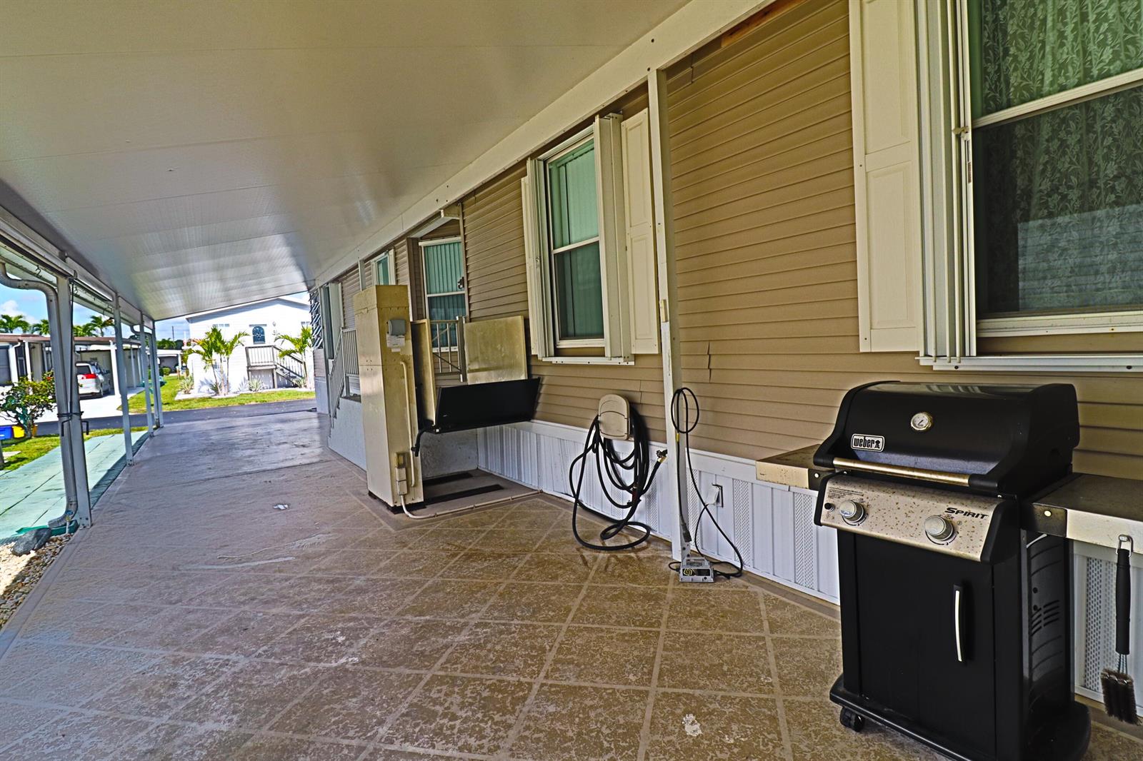 A covered patio features a wheelchair lift, a Weber grill, and beige vinyl siding — 9002 Fomento Bay, Boynton Beach FL 33436, BOYNTON BEACH, FL