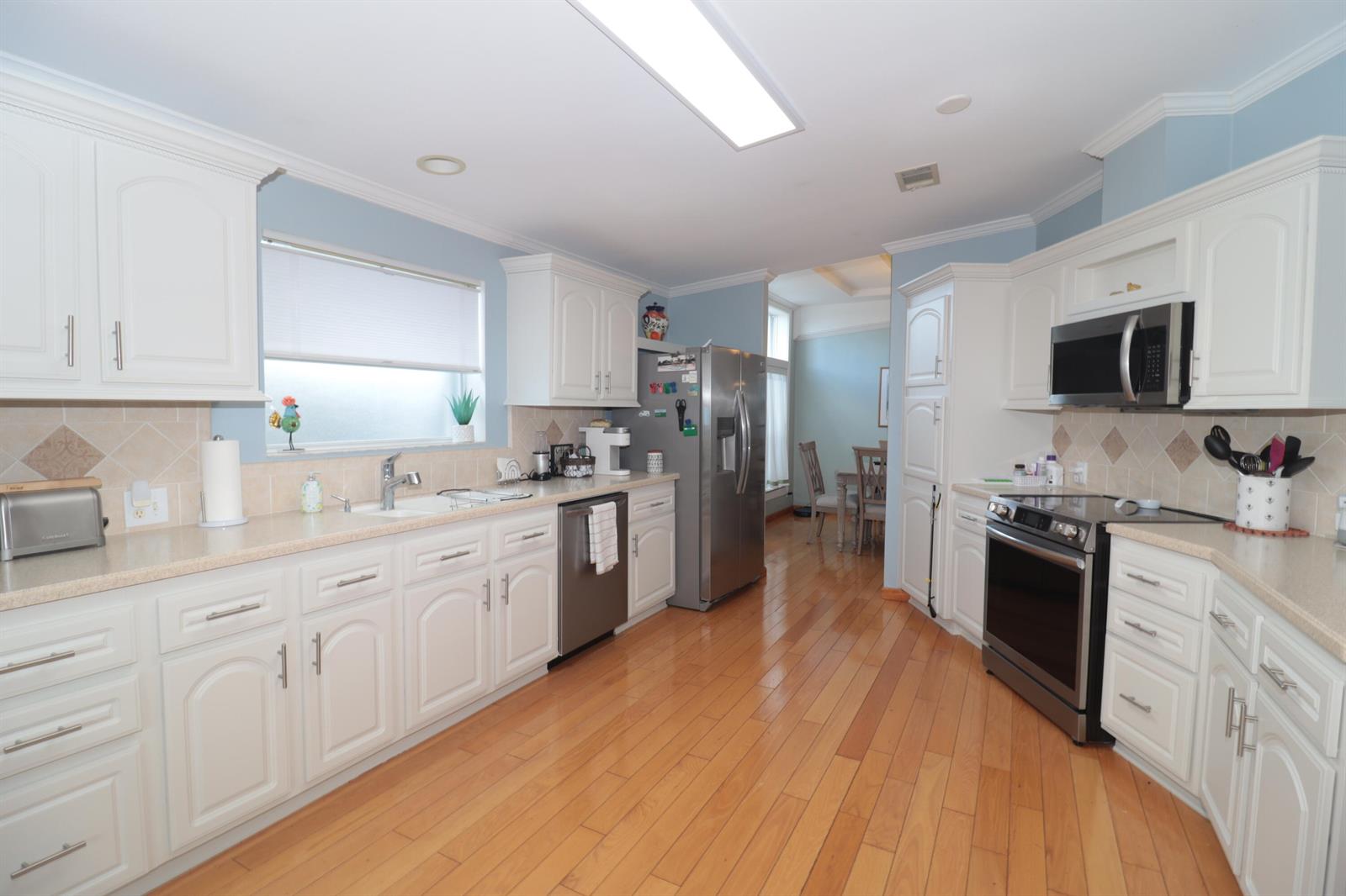 A kitchen with white cabinets, stainless steel appliances, light countertops, and hardwood flooring — 9002 Fomento Bay, Boynton Beach FL 33436, BOYNTON BEACH, FL