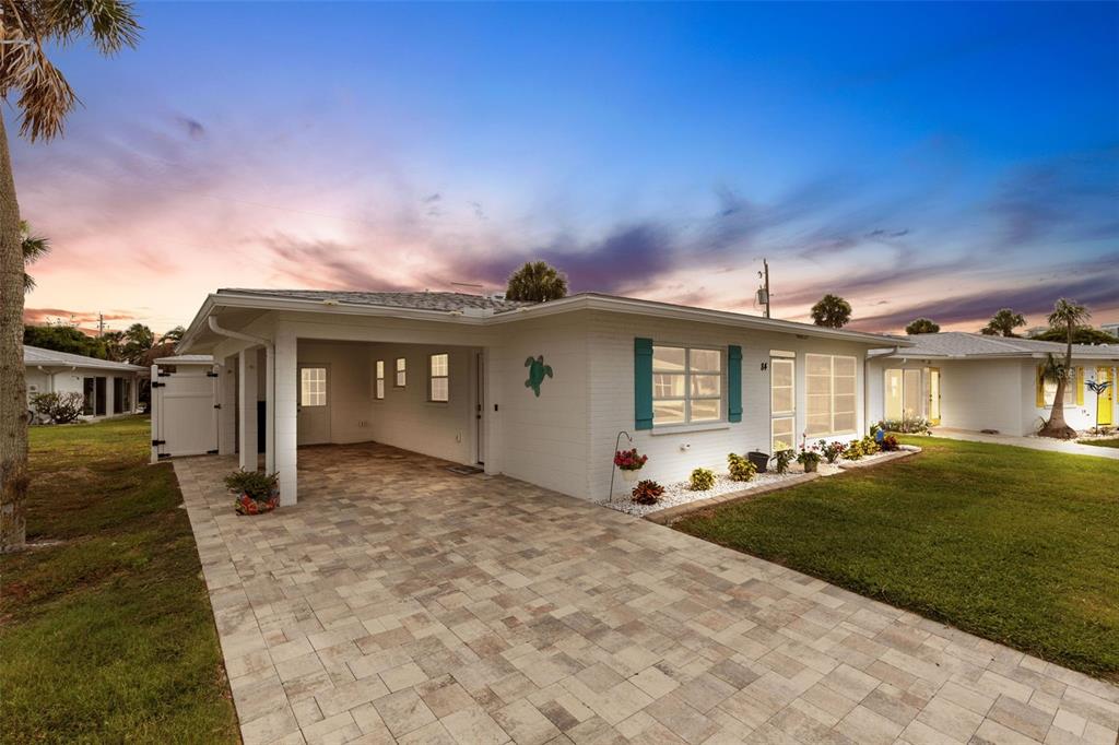 A white single-story house with a paved driveway, carport, and a green turtle wall decoration — 1977 BEACH ROAD UNIT 84, ENGLEWOOD, FL