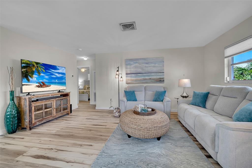 A living room features light wood flooring, a television on a wooden console, and sofas — 1977 BEACH ROAD UNIT 84, ENGLEWOOD, FL