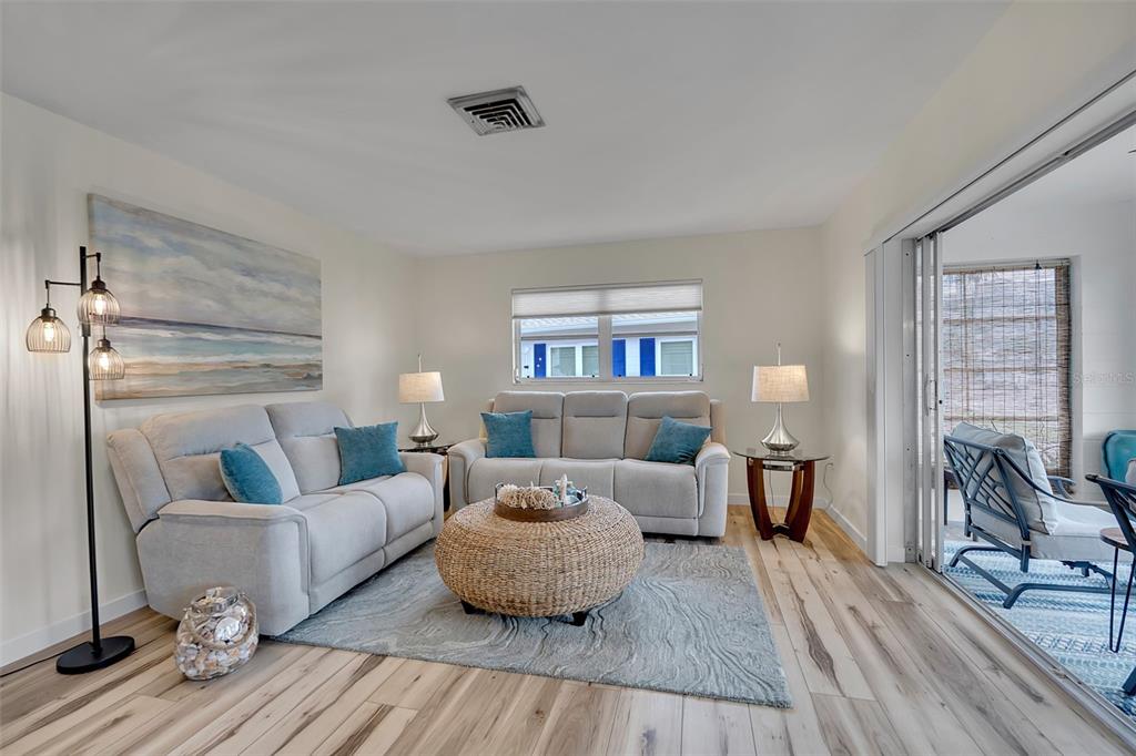 A living room features light gray sofas, a round woven coffee table, and wood-look flooring — 1977 BEACH ROAD UNIT 84, ENGLEWOOD, FL