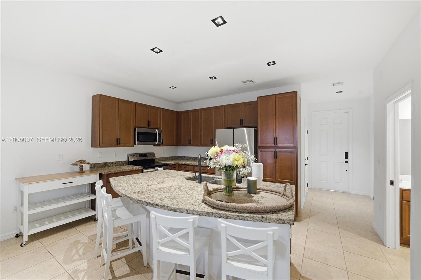 A kitchen features wood cabinets, granite countertops, a curved island, and white bar stools — 6320 S Station Sq, Davie FL 33314, DAVIE, FL