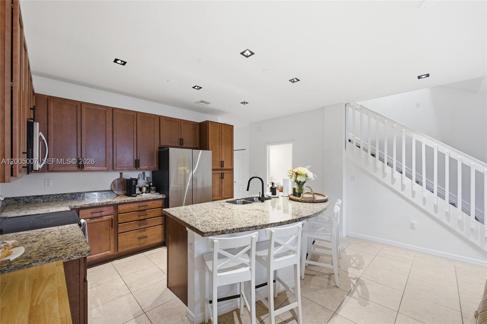 A kitchen features wood cabinets, granite countertops, a central island, and a white staircase — 6320 S Station Sq, Davie FL 33314, DAVIE, FL