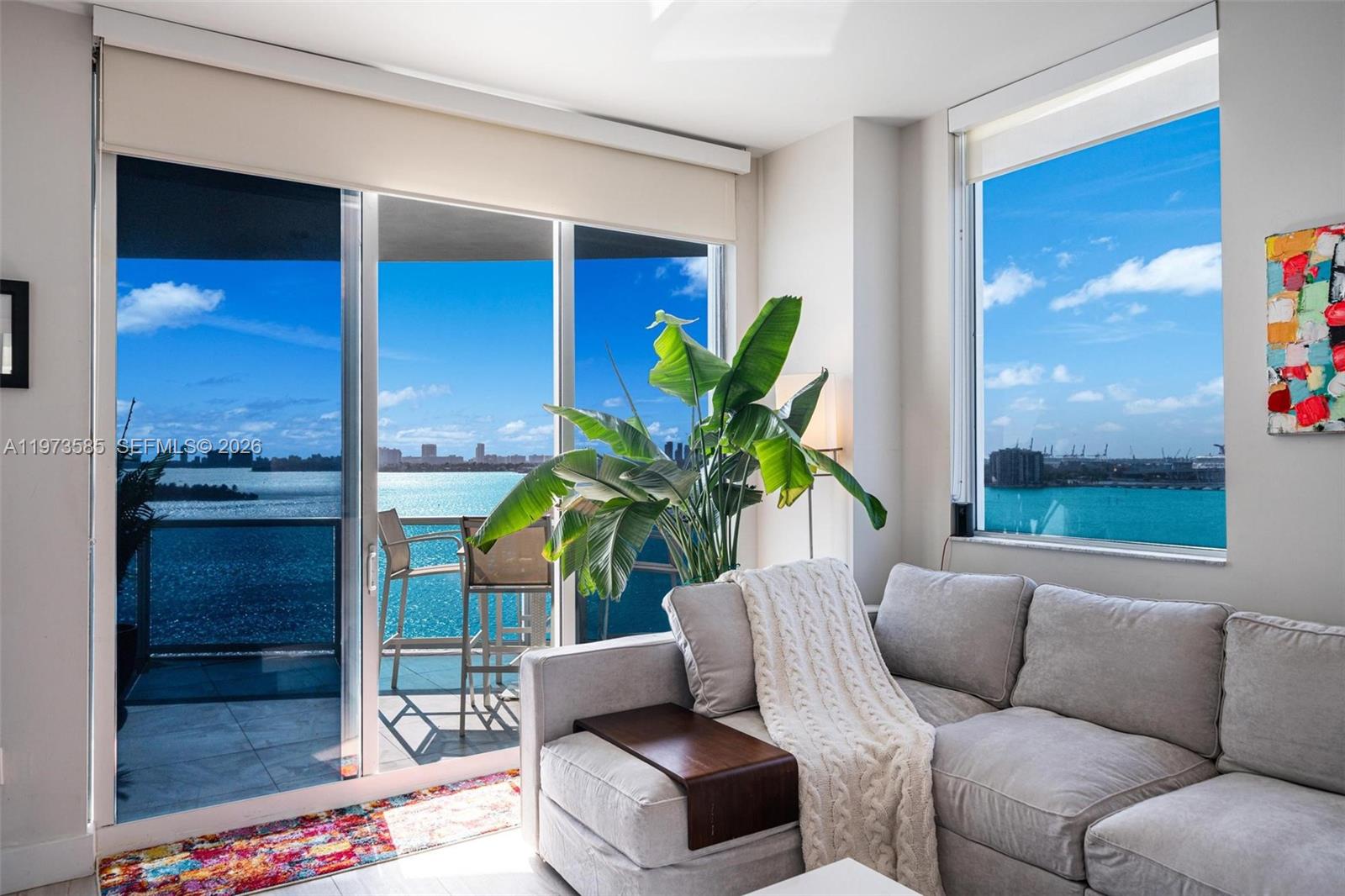 A living room features a grey sofa, a large potted plant, and floor-to-ceiling water views — 725 NE 22nd St # 10A, Miami FL 33137, MIAMI, FL