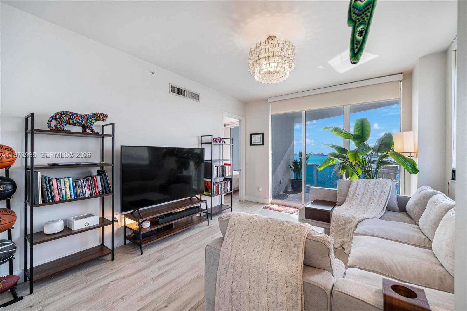 A living room features a television, bookshelves, a sectional sofa, and a balcony with water views — 725 NE 22nd St # 10A, Miami FL 33137, MIAMI, FL