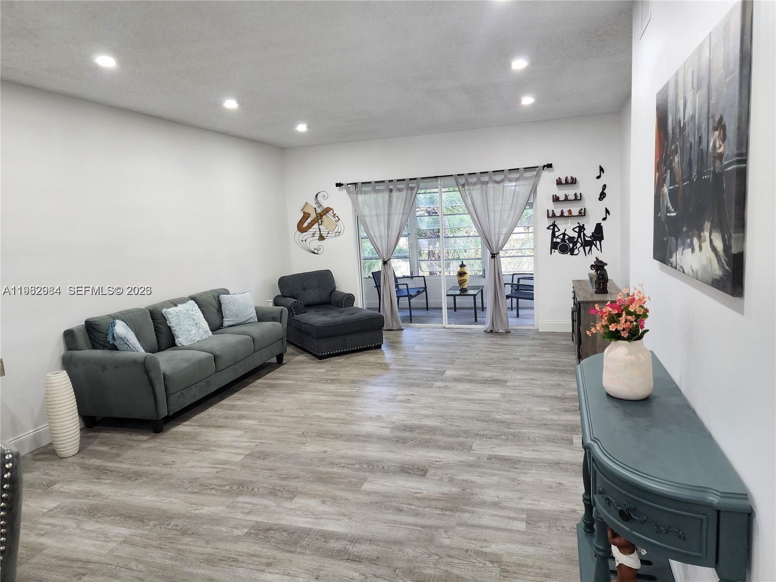A living room features gray flooring, a dark sofa, a chaise, and sliding glass doors — 7605 NW 4th Pl # 206, Margate FL 33063, MARGATE, FL
