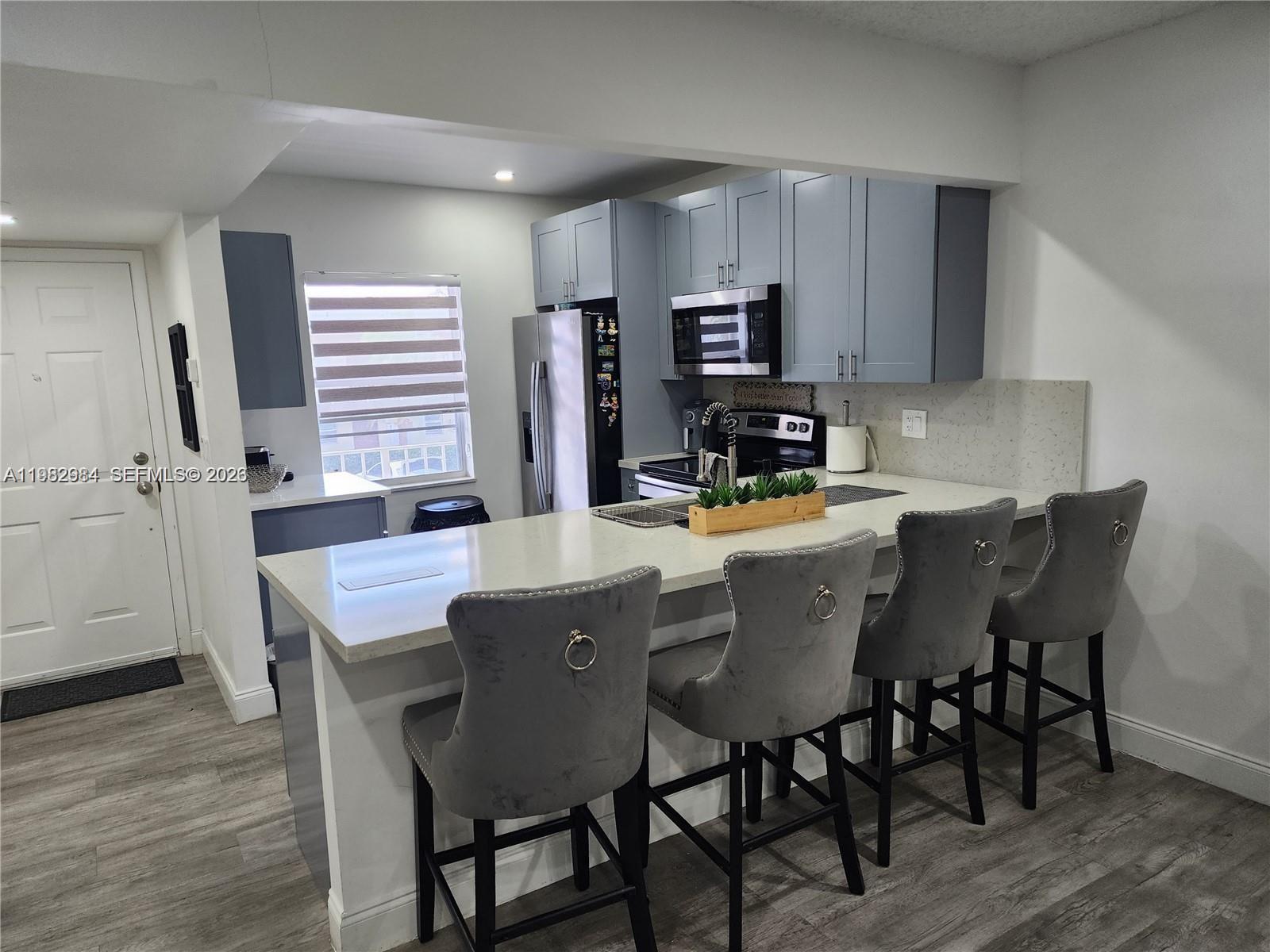 A kitchen features gray cabinets, a white quartz breakfast bar, and four gray upholstered stools — 7605 NW 4th Pl # 206, Margate FL 33063, MARGATE, FL