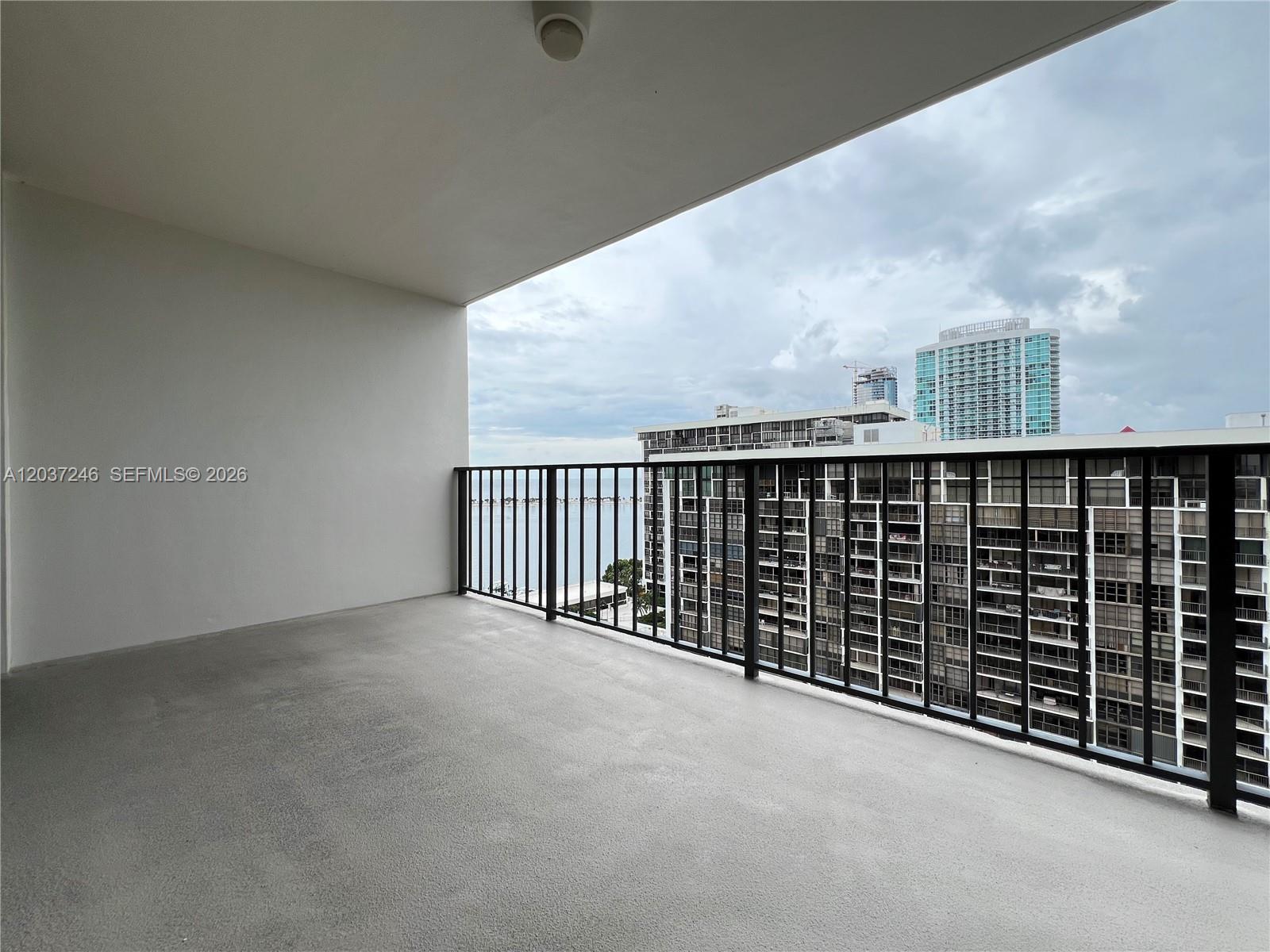 A balcony with a gray concrete floor and black metal railing overlooks a city skyline — 1901 Brickell Ave # B1807, Miami FL 33129, MIAMI, FL