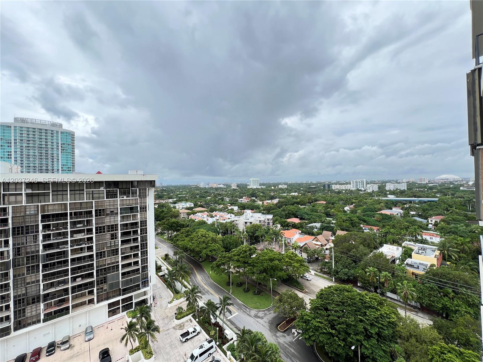 An elevated view shows a city street, lush trees, and residential buildings under a cloudy sky — 1901 Brickell Ave # B1807, Miami FL 33129, MIAMI, FL