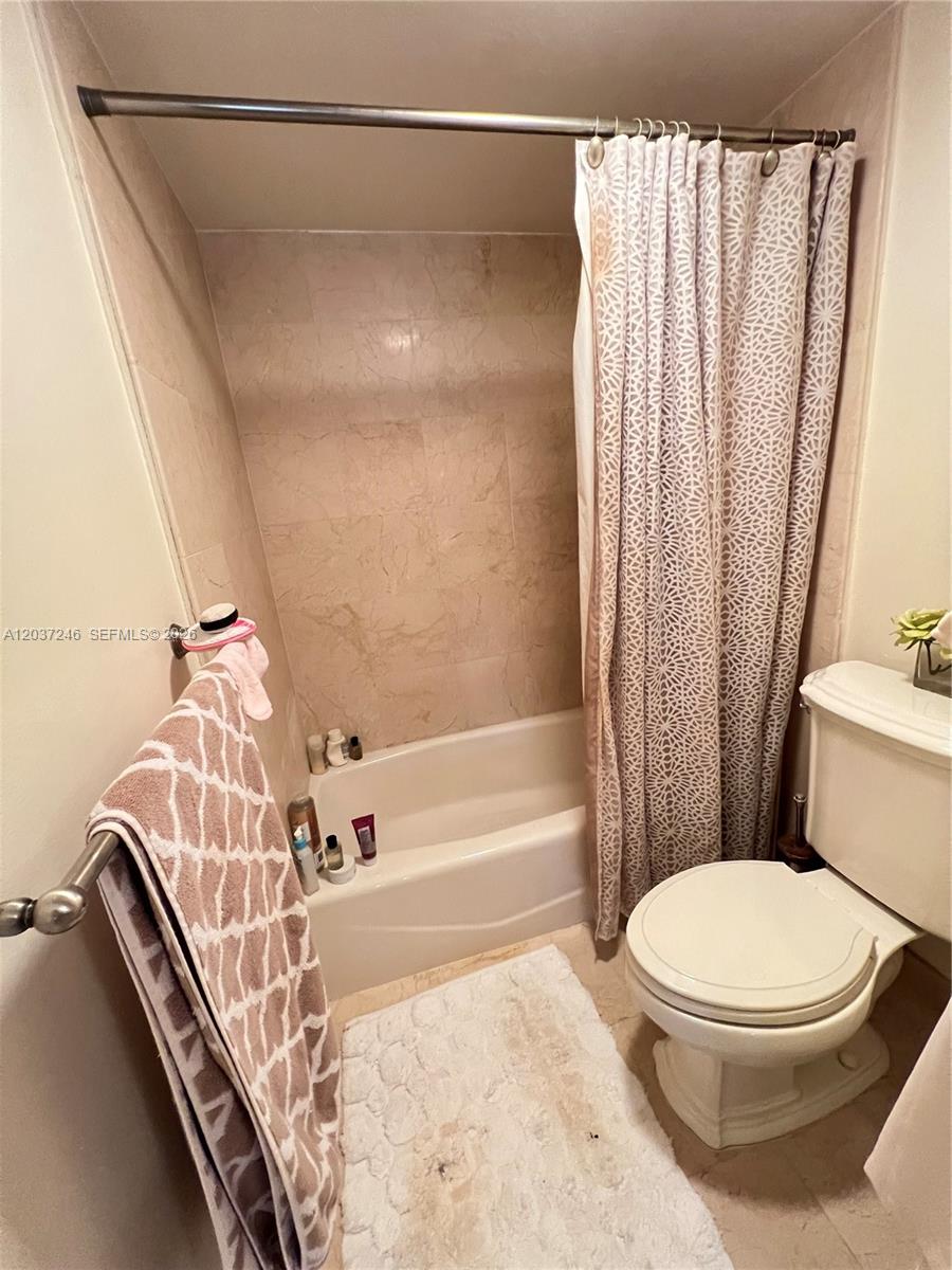A bathroom features a beige tiled shower-tub combination, a white toilet, and a patterned shower curtain — 1901 Brickell Ave # B1807, Miami FL 33129, MIAMI, FL