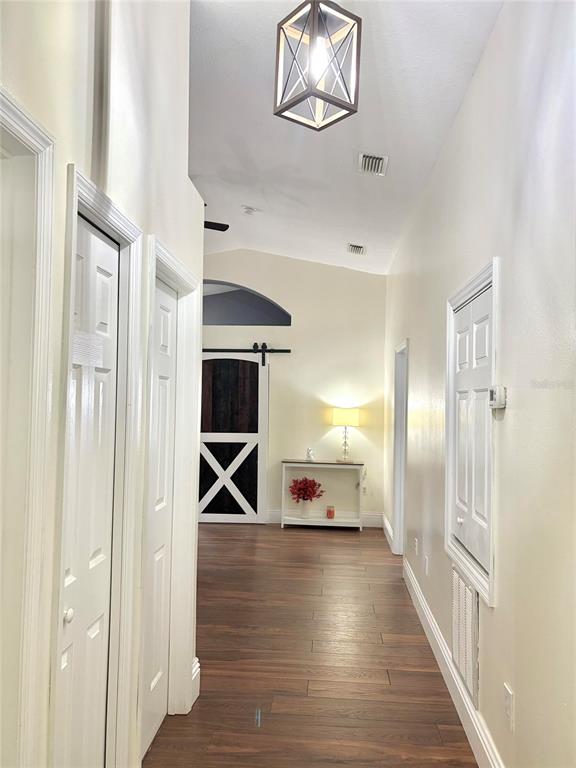 A hallway with wood-look flooring leads to a room featuring a sliding barn door — 6436 FIG LEAF STREET, ST CLOUD, FL