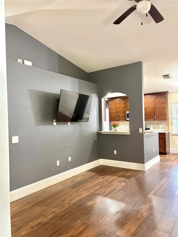 A living room features a wall-mounted television, gray walls, and wood-look flooring — 6436 FIG LEAF STREET, ST CLOUD, FL