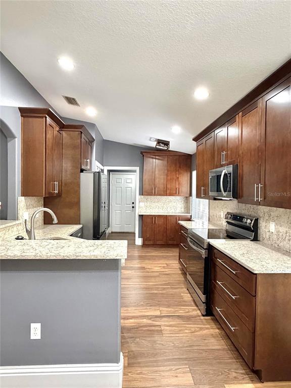 A kitchen features dark wood cabinets, light countertops, stainless steel appliances, and wood-look flooring — 6436 FIG LEAF STREET, ST CLOUD, FL