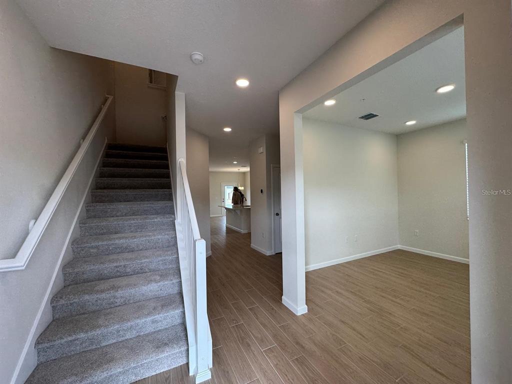 A carpeted staircase leads upward next to a room with wood-look tile flooring — 486 LADY PALM STREET, APOPKA, FL