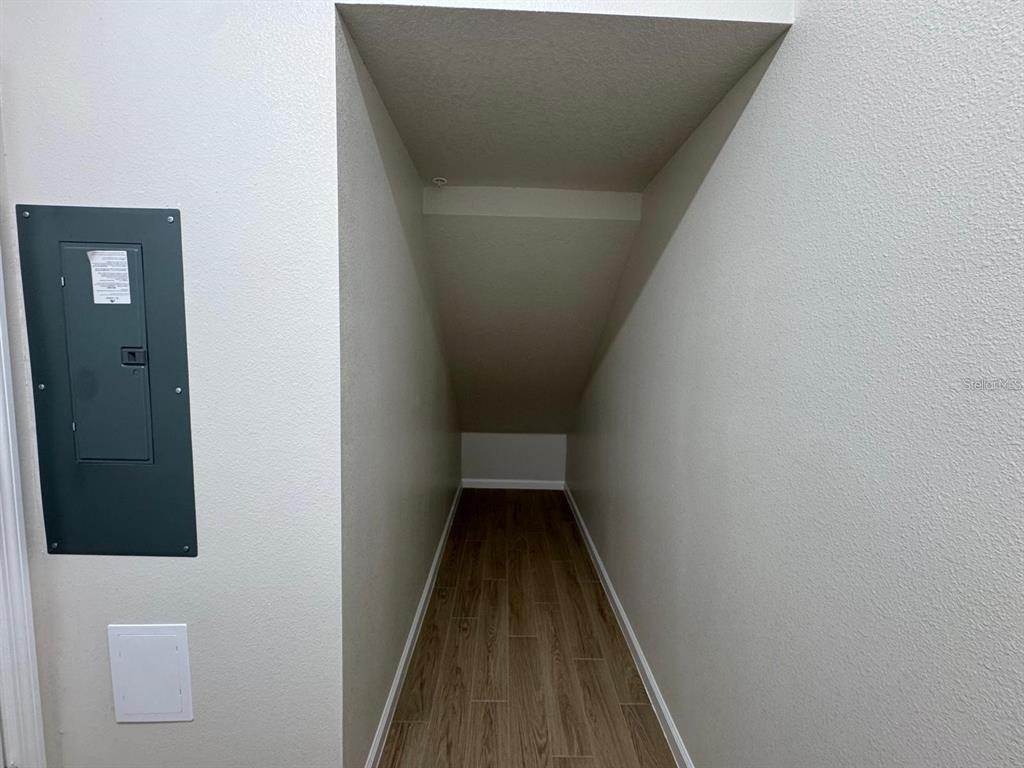 A narrow under-stair storage closet with wood-look tile flooring and a gray electrical panel — 486 LADY PALM STREET, APOPKA, FL