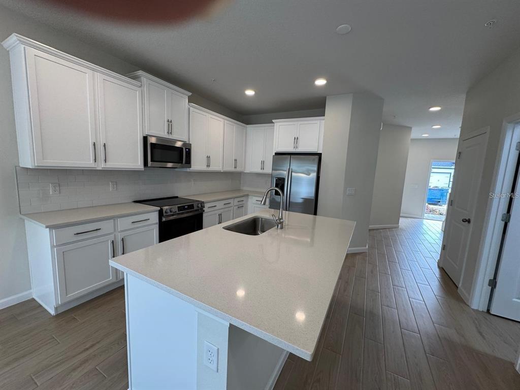 A modern kitchen features white cabinetry, quartz countertops, a center island, and wood-look tile flooring — 486 LADY PALM STREET, APOPKA, FL