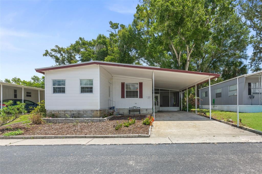 A single-story mobile home features white siding, a stone base, and an attached carport — 15601 LAKESHORE VILLA LOOP, TAMPA, FL