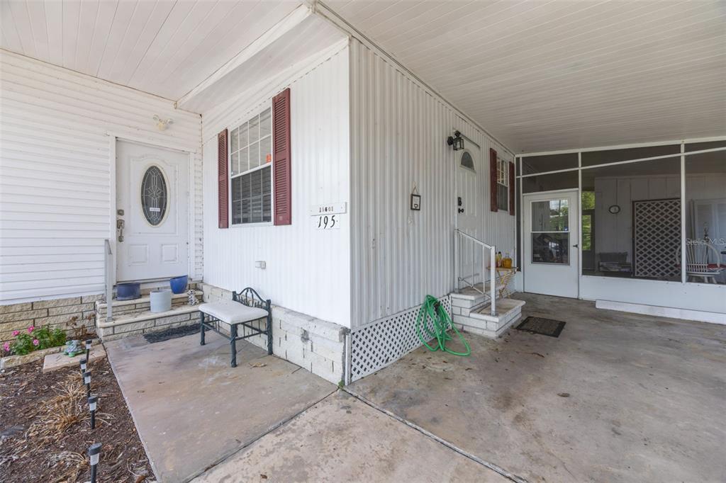 A white mobile home exterior features a concrete carport, a screened porch, and two entry doors — 15601 LAKESHORE VILLA LOOP, TAMPA, FL