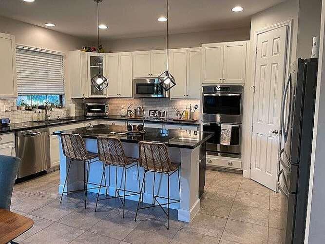 A kitchen features white cabinets, black countertops, a center island with bar stools, and appliances — 7430 NW 109th Way, Parkland FL 33076, PARKLAND, FL