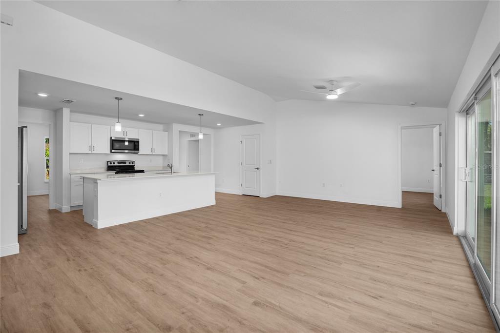 An open-concept kitchen and living area features white cabinetry, a center island, and wood-look flooring — 4529 RHAPSODY AVENUE, NORTH PORT, FL