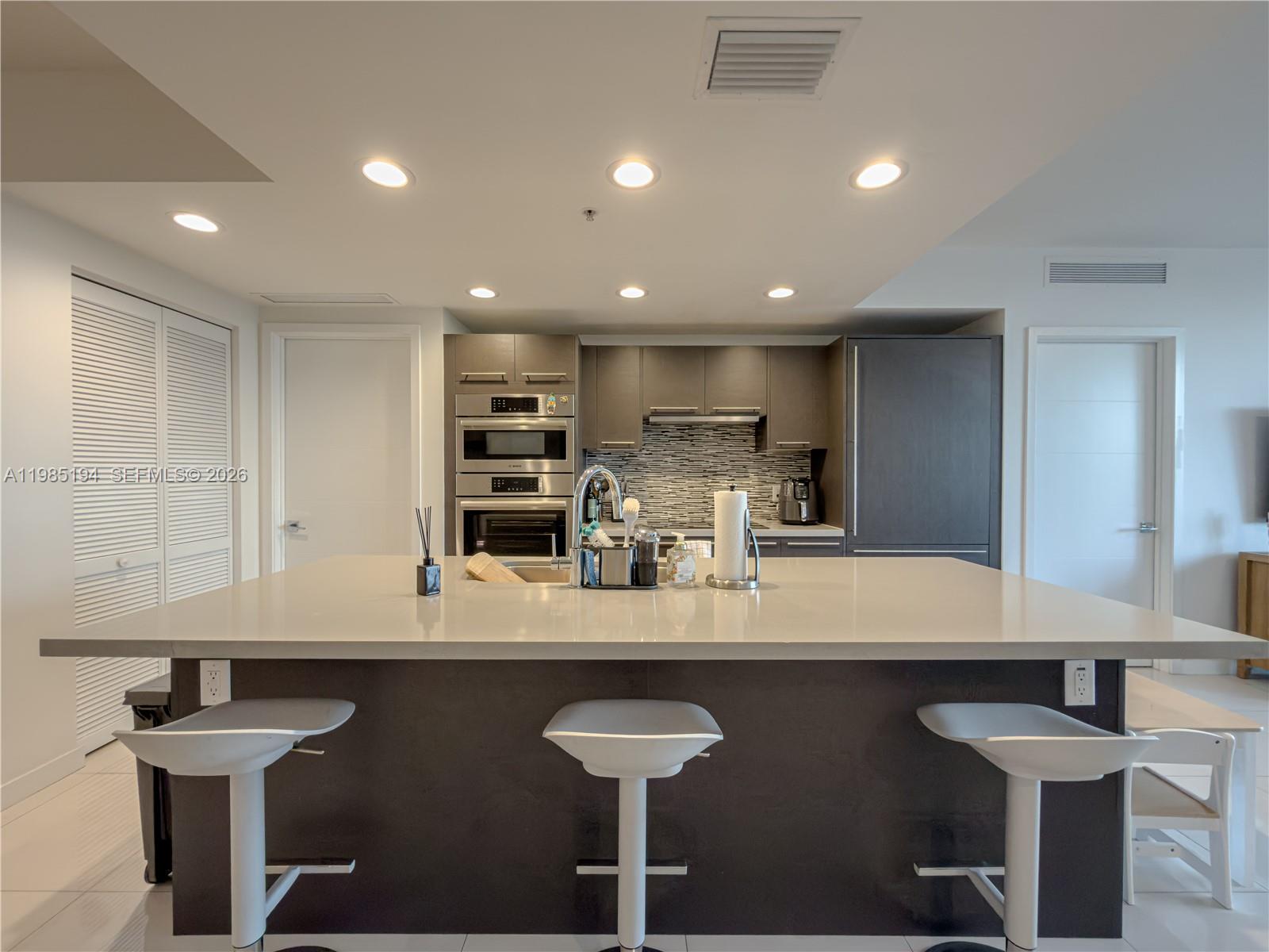 A modern kitchen features a large central island with bar seating and dark cabinetry — 7825 NW 107th Ave # 301, Doral FL 33178, DORAL, FL