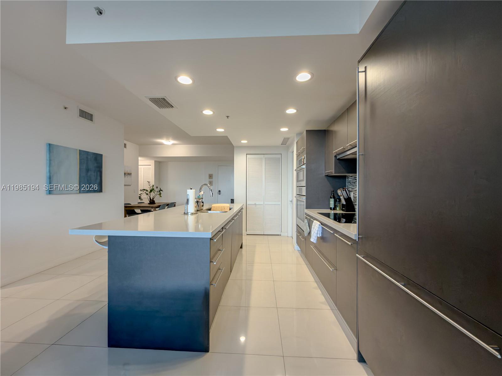 A modern kitchen features dark cabinetry, a large central island, and white tile flooring — 7825 NW 107th Ave # 301, Doral FL 33178, DORAL, FL
