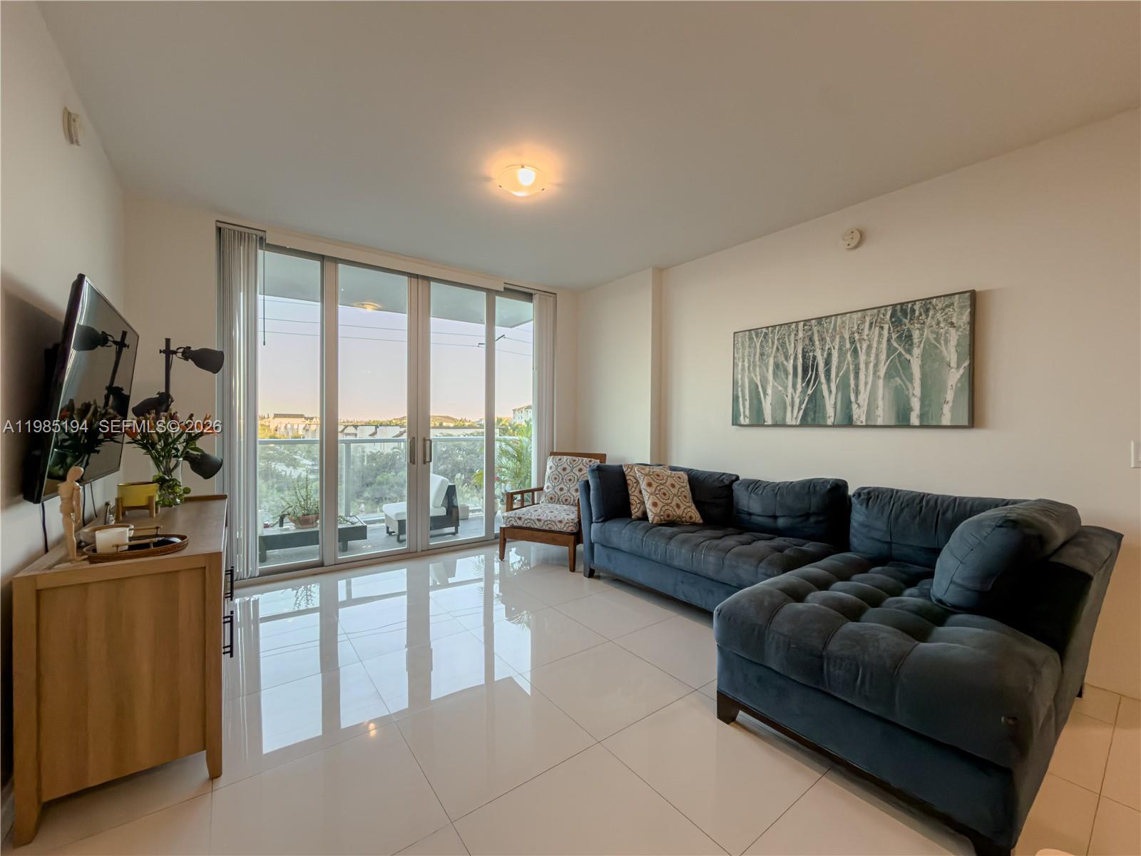 A living room features a dark blue sectional sofa, a television, and floor-to-ceiling glass doors — 7825 NW 107th Ave # 301, Doral FL 33178, DORAL, FL