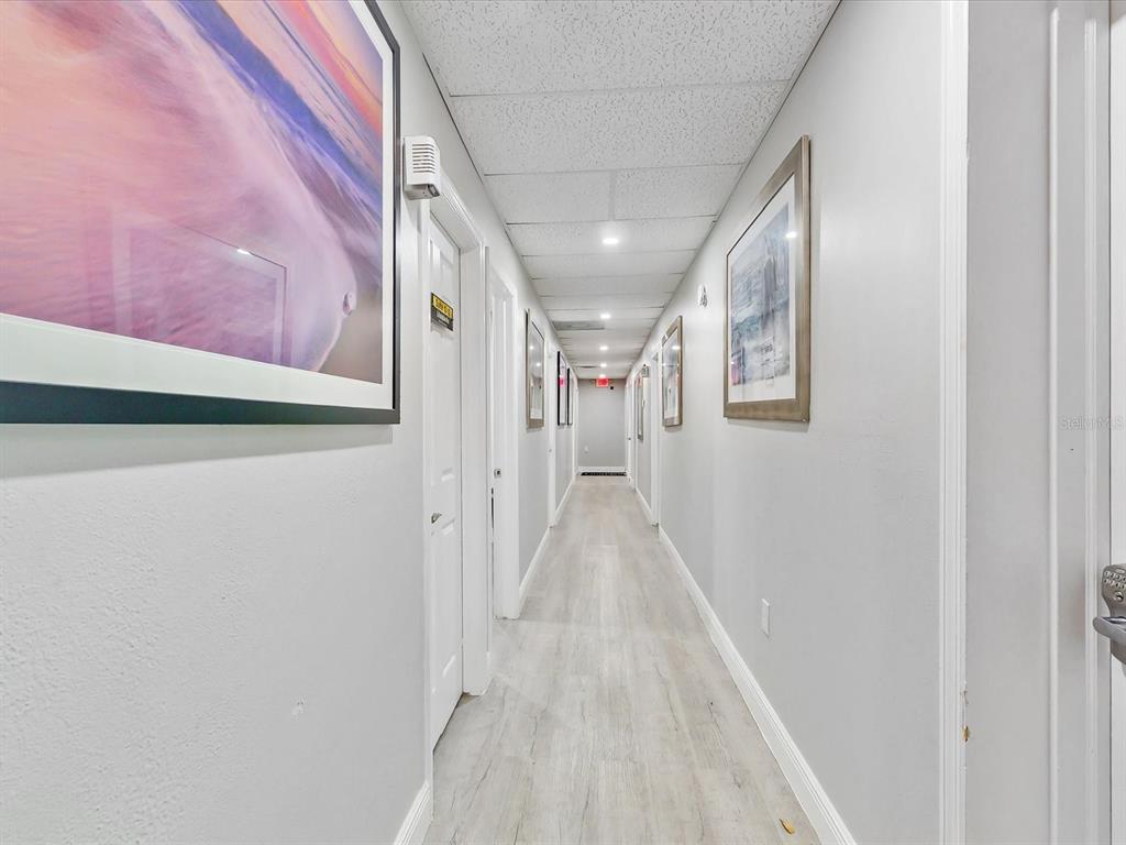 A long, narrow hallway features light-colored wood-look flooring, white walls, and framed artwork — 18 W BASS STREET, KISSIMMEE, FL