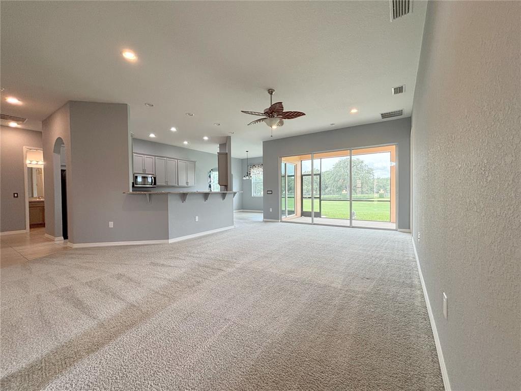A spacious living area with beige carpeting, a kitchen island, and sliding glass doors — 1124 SAWGRASS DRIVE, WINTER HAVEN, FL