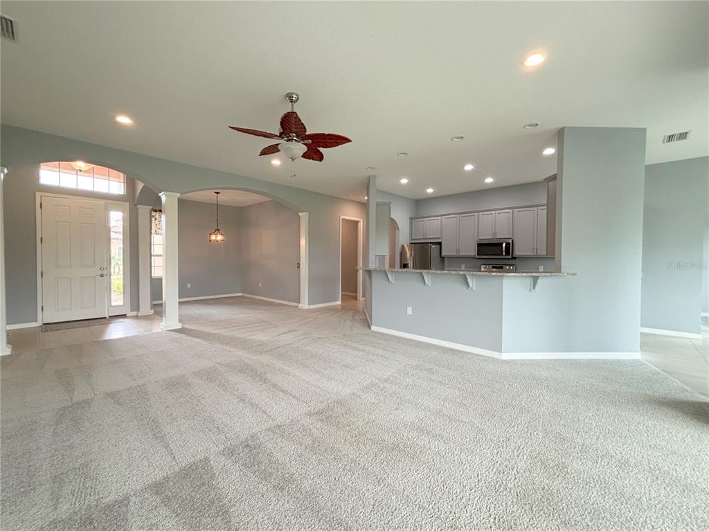 An open-concept living area features carpeted flooring, a kitchen with gray cabinets, and arched entryways — 1124 SAWGRASS DRIVE, WINTER HAVEN, FL