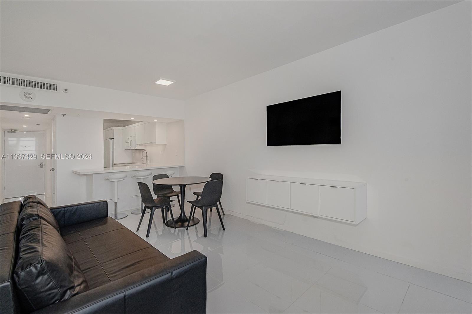 A minimalist living room features white walls, glossy tile floors, a black sofa, and a dining area — 100 Lincoln Rd # 519, Miami Beach FL 33139, MIAMI BEACH, FL