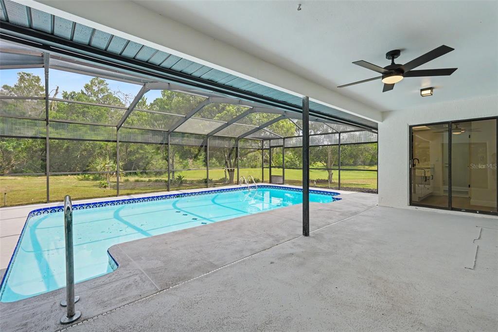 A covered patio with a ceiling fan overlooks a screened-in swimming pool and backyard — 6444 CROWLEY COURT, SPRING HILL, FL