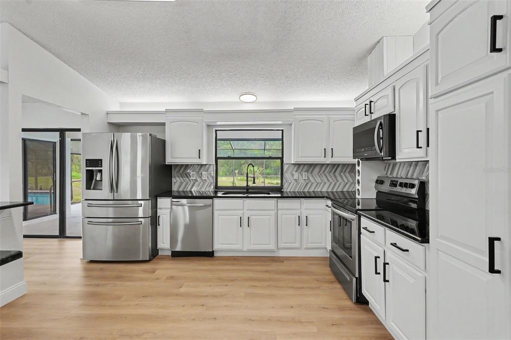 A kitchen features white cabinets, black countertops, stainless steel appliances, and light wood flooring — 6444 CROWLEY COURT, SPRING HILL, FL
