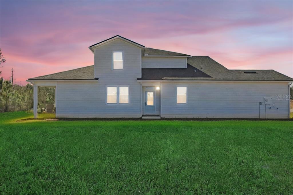 A two-story white house with a shingled roof stands behind a large green lawn — 18 BIG PINE DRIVE, PALM COAST, FL