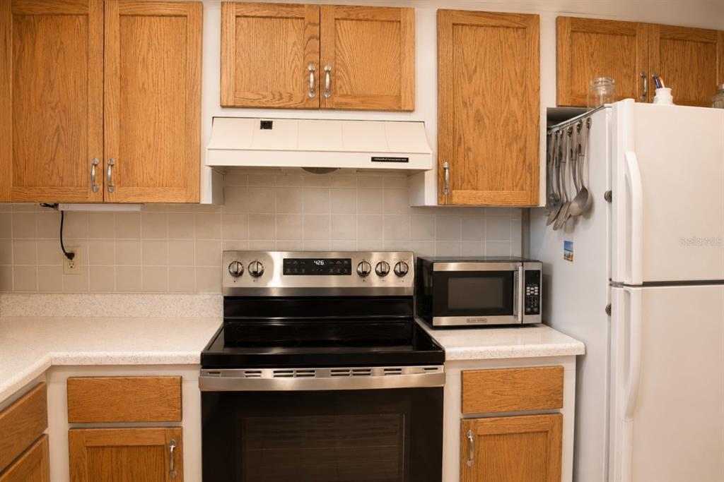 A kitchen features oak cabinets, a stainless steel stove, a microwave, and a white refrigerator — 1662 S LAKE AVENUE UNIT 6, CLEARWATER, FL