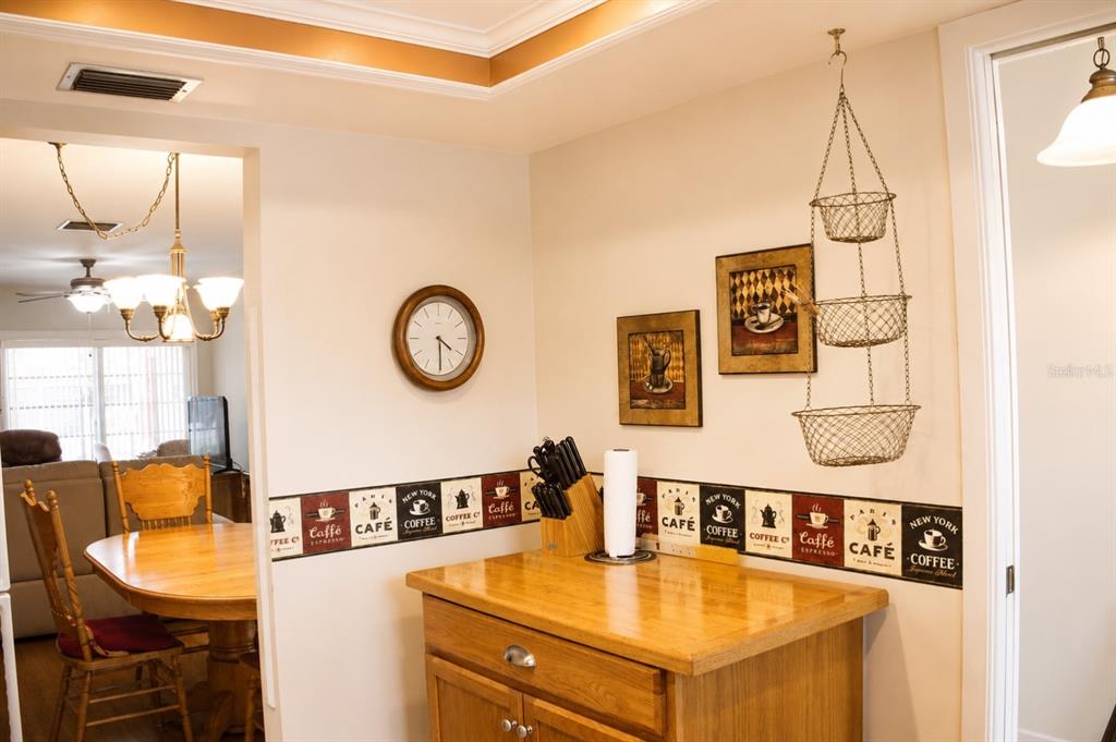 A kitchen area features a wooden island, coffee-themed wallpaper border, wall clock, and hanging baskets — 1662 S LAKE AVENUE UNIT 6, CLEARWATER, FL