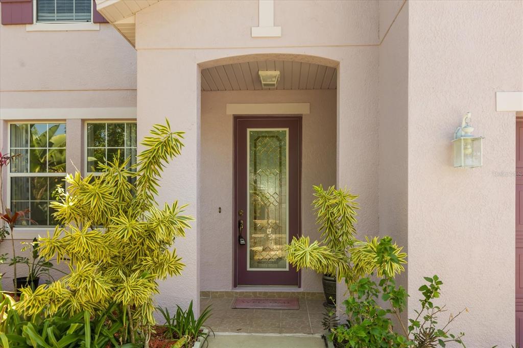 A front entryway features a purple door with a glass insert and surrounding tropical plants — 402 CHIMNEY ROCK DRIVE, RUSKIN, FL