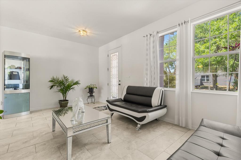 A bright living room features white walls, tile flooring, a mirrored coffee table, and seating — 402 CHIMNEY ROCK DRIVE, RUSKIN, FL