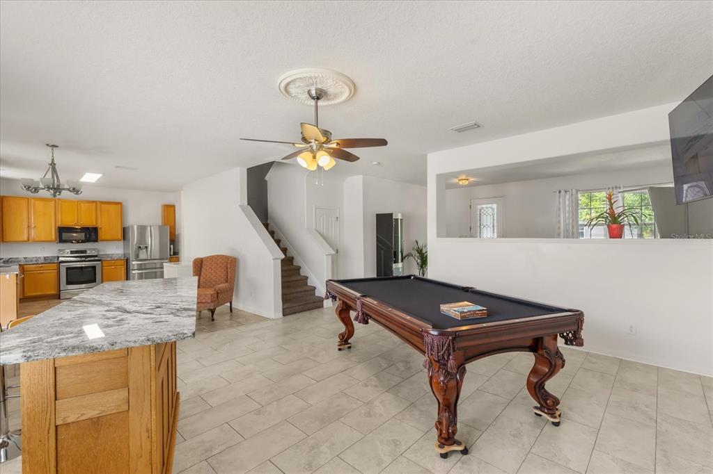 A kitchen with wood cabinets and a granite island opens to a room with a pool table — 402 CHIMNEY ROCK DRIVE, RUSKIN, FL