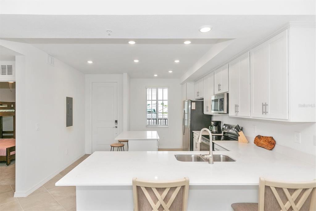 A bright kitchen features white cabinets, quartz countertops, a breakfast bar, and stainless steel appliances — 12320 WELLEN GOLF STREET UNIT 204, VENICE, FL