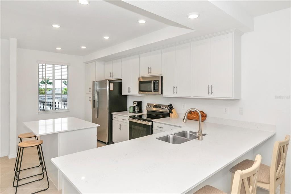 A modern kitchen features white cabinets, stainless steel appliances, and a white quartz island — 12320 WELLEN GOLF STREET UNIT 204, VENICE, FL