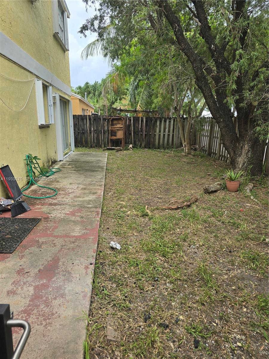 A concrete patio runs alongside a yellow house with a fenced backyard and trees — 12687 SW 146th St, Miami FL 33186, MIAMI, FL