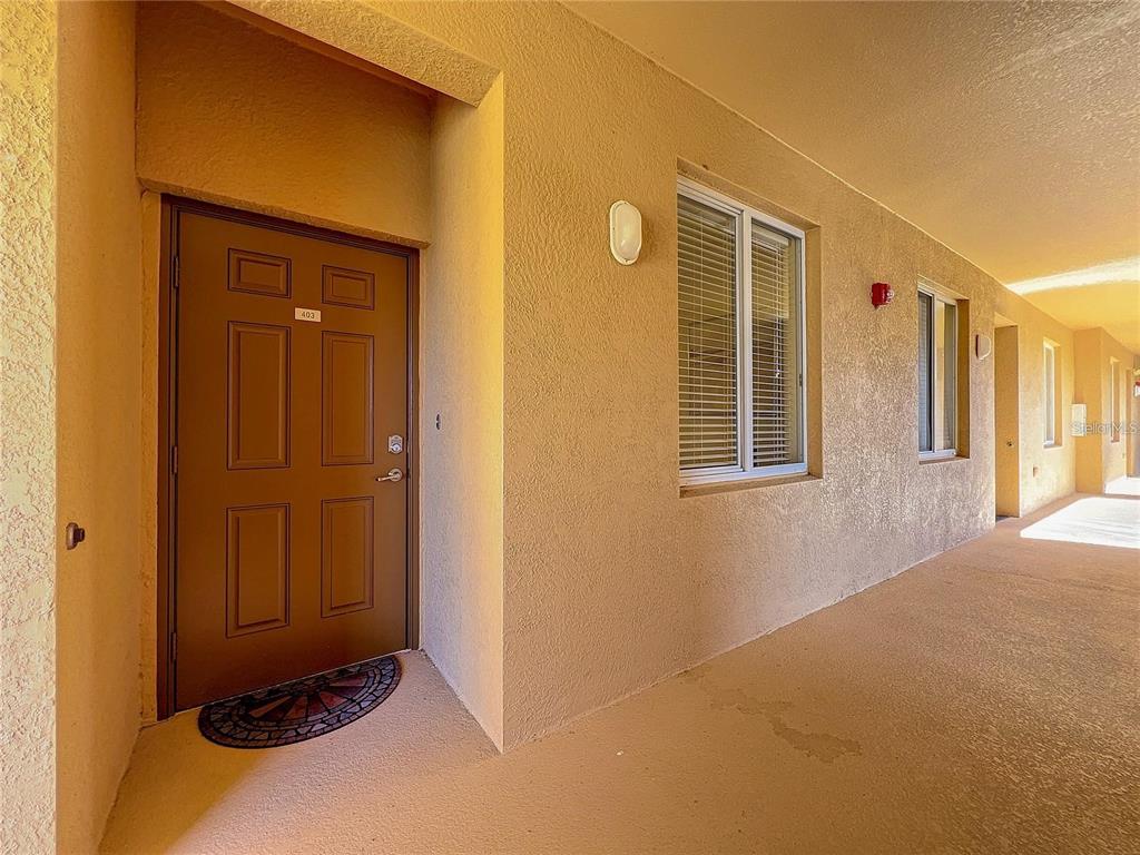 A brown front door with the number 403 is set in a tan stucco exterior hallway — 8205 GRAND ESTUARY TRAIL UNIT 403, BRADENTON, FL