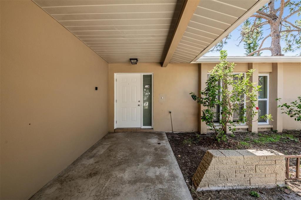 A covered concrete entryway leads to a white front door with a side window panel — 1124 DANNY DRIVE, SARASOTA, FL